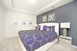 Enjoy a tranquil bedroom featuring a chic upholstered bed with a stunning purple and gray geometric duvet. Stylish lamps cast a warm light, while unique artwork adds character to the sleek walls, making it a perfect retreat.