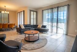 Relax in a bright living room with a black leather sectional, soft gray curtains, round coffee table, cozy accent chair, pool views, and nearby dining area, creating a comfortable space for vacation moments.