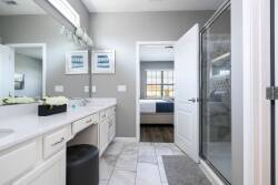 Experience the inviting bathroom with sleek white cabinetry and a spacious double vanity, perfect for relaxation. The neutral gray walls and natural light create a refreshing ambiance, seamlessly leading to a cozy bedroom beyond.