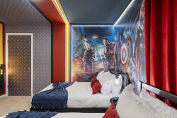 Rest in a bold superhero themed bedroom with two comfortable beds, vibrant wall art, red accents, and fun lighting. The dramatic decor creates an exciting space for kids and fans to enjoy during their vacation.