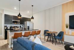 Experience a stylish kitchen and dining area featuring sleek black cabinetry and warm wood accents. Cook with modern stainless appliances and enjoy meals at a chic dining table, beautifully lit by contemporary pendant lights.