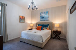 Enter a serene retreat with plush carpeting and a lovely queen bed dressed in colorful accent pillows. The soft glow from chic bedside lamps and an elegant chandelier sets a warm atmosphere ideal for your relaxation.