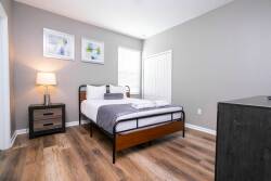 Bright and airy, this bedroom features warm wood flooring that complements the sleek metal bed frame and crisp white linens. Two modern artworks adorn the walls, while the bedside lamp casts a cozy glow for relaxed evenings.