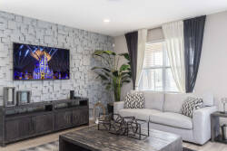 Unwind in the cozy living room featuring a plush gray sofa and a chic stone accent wall. Large windows dressed with elegant curtains fill the space with natural light, creating the perfect setting for relaxation or a movie night.