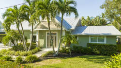 Welcome to a vibrant oasis of palm trees and tropical landscaping. The charming entrance, with its soft green hues and stylish peaked roof, invites you to embrace your next adventure in this perfect indoor-outdoor setting.