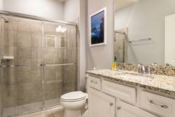 Freshen up in a clean bathroom with a glass walk-in shower, granite vanity, large mirror, white cabinets, soft lighting, and neutral tones, offering comfort during vacation.