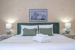 Unwind in this beautifully designed bedroom with a plush green headboard against warm, textured walls. Elegant lamps cast a soft glow over crisp white linens, creating a cozy and inviting atmosphere just for you.