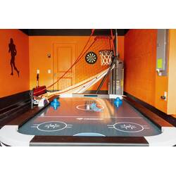 Have fun in a vibrant game room with an air hockey table, basketball arcade game, dart board, bold orange walls, and sporty decor for relaxed family entertainment.