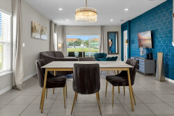Discover a stylish dining area featuring a striking blue wall and a chic chandelier, where modern chairs surround a sleek table. Large windows invite natural light, creating a warm and inviting atmosphere for your meals.