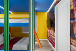 This vibrant room features a colorful bunk bed with a blue top and green frame against a sunny yellow wall. The playful mural adds a unique touch, creating an energetic atmosphere ideal for relaxation and fun.