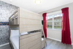Bright red curtains frame a cozy room featuring a stylish wooden bunk bed, perfect for families or friends. The playful wallpaper adds a touch of whimsy, while ample natural light streams in, creating a cheerful atmosphere.