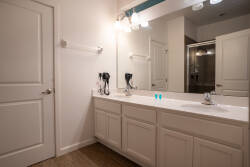 Refresh in a spacious bathroom with a long double vanity, large mirror, bright lighting, and a glass-enclosed shower. Neutral tones, clean finishes, and wood-look floors create a comfortable space for your vacation.