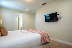 Experience comfort in this cozy bedroom, featuring a plush white bed dressed with a soft, blush throw. A sleek, wall-mounted TV offers entertainment options, while warm lighting creates a welcoming ambiance for relaxation.