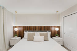 This beautifully designed bedroom offers a cozy white bed with stylish nightstands, lush greenery, and elegant pendant lights. The warm wood accent wall enhances the sophisticated, peaceful atmosphere for restful nights.