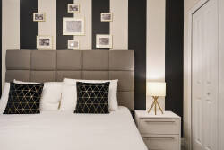 Enjoy peaceful nights in this stylish bedroom with a tufted headboard and geometric pillows. The bold black-and-white striped walls showcase framed art, while soft bedside lighting creates a warm, inviting atmosphere.