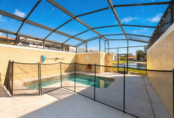 Step outside to your private pool area, surrounded by a secure mesh fence and framed by a spacious patio. The bright blue sky overhead creates a refreshing atmosphere, perfect for sunbathing or enjoying an afternoon dip.