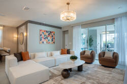 This bright and airy living room boasts a plush white sectional and cozy armchairs for a stylish yet relaxed vibe. Colorful wall art adds playfulness, while large windows flood the space with light and connect you to the outdoors.