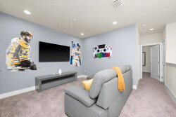 Step into this vibrant game room, where playful sports-themed murals energize the space. The plush gray sofa invites you to relax while enjoying movies on the large flat-screen TV, making it an ideal spot for family fun.