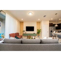 Relax in a cozy living room with a gray sofa, pink accent chairs, wall-mounted TV, wood slat details, soft white curtains, pool view, and fresh decor for vacation comfort.