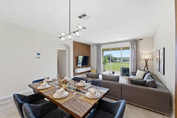 Gather in a bright open dining and living area with a set wooden table, cozy gray seating, modern lighting, wall-mounted TV, soft curtains, and sliding glass doors with peaceful balcony views.