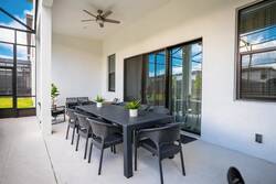 Enjoy al fresco dining in a spacious area featuring sleek dark furniture and large sliding doors that invite natural light. A ceiling fan adds a gentle breeze, creating a bright and comfortable atmosphere for your gatherings.