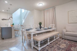This bright dining area welcomes family meals with a charming white wooden table and rustic bench, bathed in natural light that enhances the soft curtains and detailed area rug, creating a warm and inviting atmosphere.
