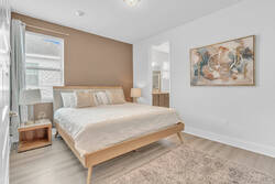 Rest in a bright bedroom with a light wood bed, soft white bedding, warm accent wall, abstract wall art, bedside lamps, cozy rug, and direct access to a private bathroom.