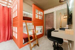 This charming room offers a vibrant orange bunk bed and warm red curtains, creating a cozy vibe. A sleek workspace with a modern chair encourages productivity, making it the perfect retreat for relaxation and work alike.