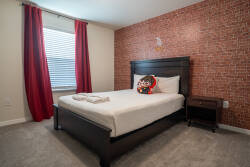 This cozy bedroom boasts a charming brick accent wall, plush carpeting, and vibrant red curtains that let in natural light. With a comfortable bed, it ensures restful nights, creating an inviting retreat for relaxation.