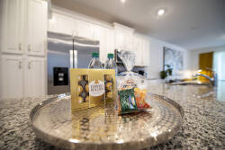Enjoy a curated welcome tray with snacks and refreshing bottled water, set against sleek white cabinetry and a sparkling granite countertop. The soft lighting creates an inviting atmosphere, perfect for starting your vacation.