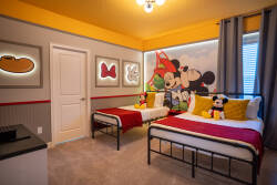 This cheerful themed bedroom offers two cozy beds with vibrant yellow and red accents and playful Mickey Mouse artwork. Soft gray carpeting and warm lighting create a welcoming atmosphere for your relaxation.