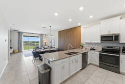 Enjoy a bright open space with a modern kitchen, large island, white cabinetry, stainless steel appliances, dining area, warm wood accent wall, and relaxing views toward the balcony.