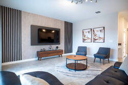 Relax in a modern living room with a black leather sofa, gray accent chairs, wall-mounted TV, wood details, soft curtains, pool views, and a round coffee table, creating a comfortable space for vacation moments.