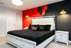 Rest in a Mickey themed bedroom with a cozy bed, bold red and black accent wall, yellow pendant lights, soft curtains, and playful character decor, creating a fun and comfortable space for vacation.