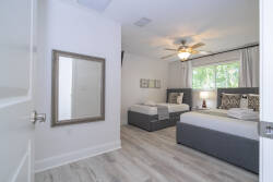 Step into a light-filled bedroom featuring two comfortable beds with stylish gray upholstered bases, perfect for restful nights. The room showcases soft wood-like flooring and a chic mirror, adding to the inviting ambiance.