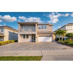 Arrive at a modern two-story home with a stone-accent facade, spacious driveway, private garage, balcony, palm trees, and bright curb appeal under the Florida sky.
