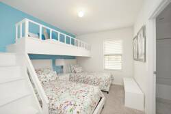 This cheerful bedroom offers a lofted bed over twin beds, ideal for families. With bright floral bedding against calming blue walls and plenty of natural light, it creates a refreshing and inviting atmosphere for guests.