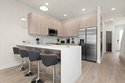 Welcome to a contemporary kitchen with sleek wood cabinetry and a spacious island with stylish bar stools, perfect for casual dining. Modern amenities and bright lighting create an inviting atmosphere for your culinary adventures.