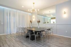 This stylish dining area boasts a sleek black table with transparent chairs, offering a chic contrast to soft gray walls. Natural light pours in through sheer curtains, creating an inviting atmosphere ideal for shared meals.