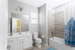This bright and airy bathroom showcases sleek white cabinetry and warm light wood floors. A refreshing blue accent on the shower curtain adds a cheerful touch, enhancing your morning routine with a vibrant atmosphere.