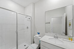 Freshen up in a bright bathroom with a glass walk-in shower, white tile walls, large mirror, clean vanity, soft towels, and simple modern details for a comfortable stay.