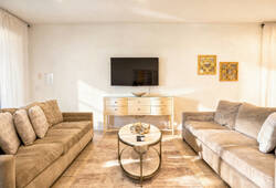This bright living room features two cozy gray sofas, a chic coffee table, and stylish decor. With natural light streaming through large windows, it creates a warm atmosphere, making it the ideal place to relax and unwind.