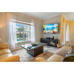 This cozy living room, bathed in natural light, features soft cream sofas and a stylish dark wood coffee table. A large flat-screen TV awaits your movie nights, while sheer curtains bring a touch of elegance to the space.