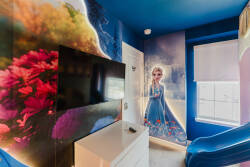 Experience the charm of this whimsical bedroom, featuring rich blue walls with enchanting artwork that create a playful vibe. Enjoy cozy moments in the plush seating, complemented by sleek white furniture for a modern touch.