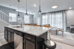 This stylish kitchen boasts a striking granite island and sleek black cabinetry, ideal for casual dining. Soft gray walls and ample natural light from large windows create an uplifting atmosphere for your culinary adventures.