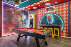 Play in a colorful Super Mario game room with a pool table, arcade machine, fun wall art, bright lighting, and bar stools, creating a lively space for family entertainment during vacation.