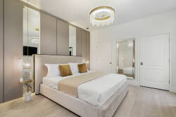 Experience a cozy atmosphere in this beautifully designed bedroom with a plush bed, neutral linens, and golden accents. Modern elegance is highlighted by sleek cabinetry, a stylish chandelier, and bright mirrored surfaces for a.
