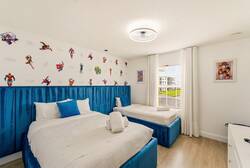 This vibrant bedroom features fun superhero wallpaper and cozy twin beds with crisp white linens and bright blue accents. Sunlight streams through large windows, making it a cheerful space perfect for memorable adventures.