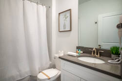 Experience this beautifully designed bathroom with a sleek dark countertop and light cabinetry. The soft white shower curtain and tasteful decor create a refreshing atmosphere, ideal for relaxation and unwinding.