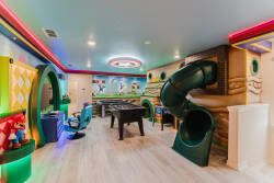 Discover a vibrant playroom adorned with cheerful murals and colorful LED lights. A thrilling slide adds fun, and a sleek foosball table invites friendly competition, creating the perfect space for kids and the young at heart.